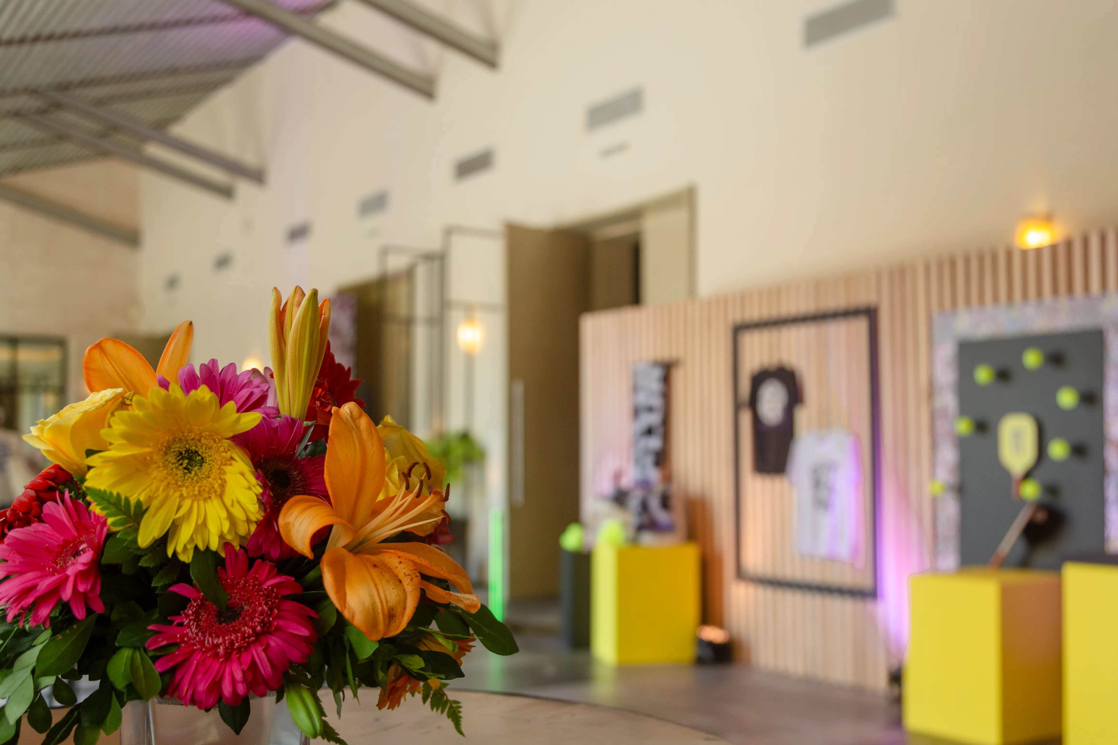 Close-up of orange and pink tropical flowers in a hotel foyer, with colorful arrival displays in the background.