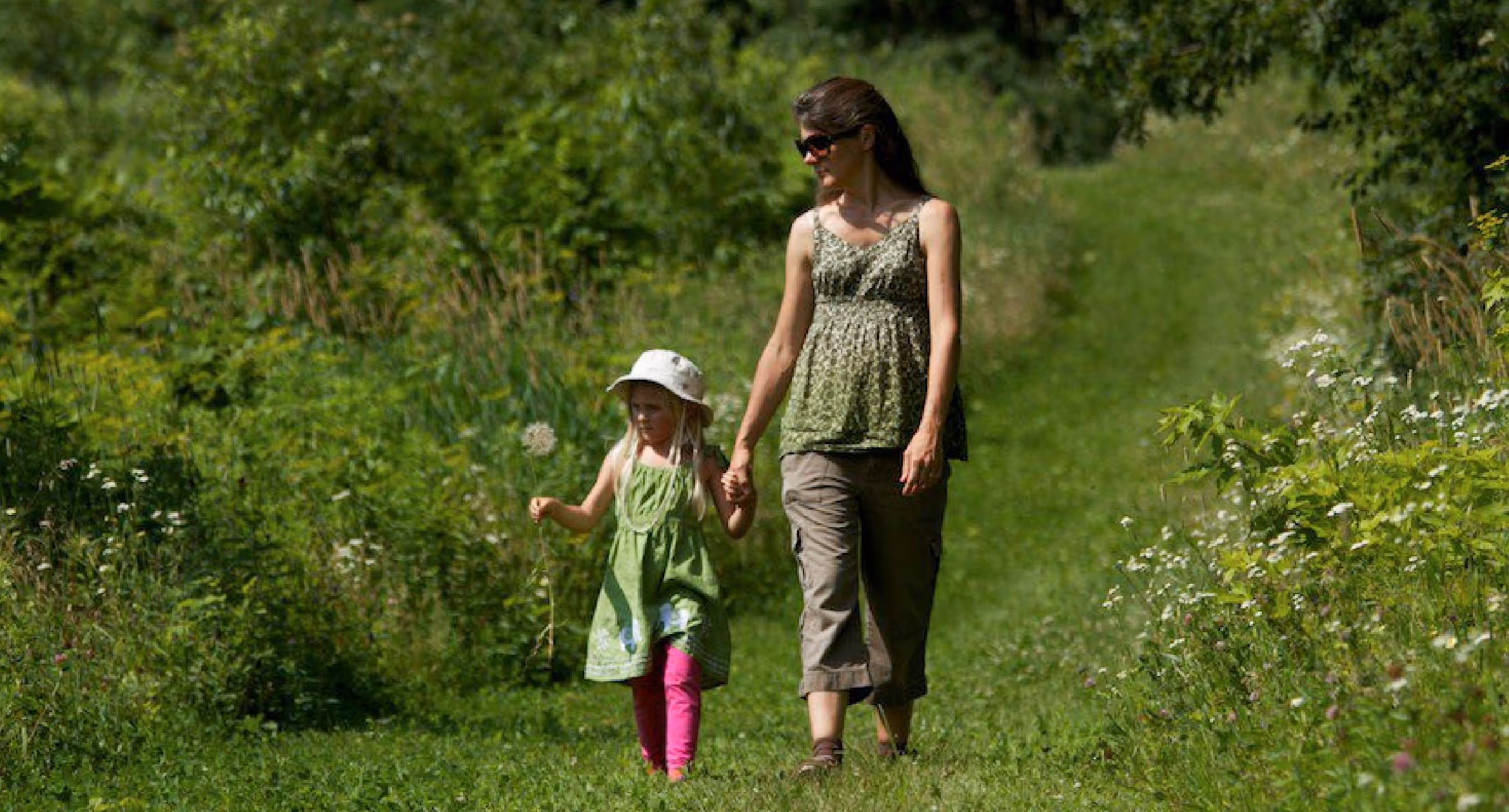 Teresa walking hand in hand with her daughter Kacia through a grassy field surrounded by trees.