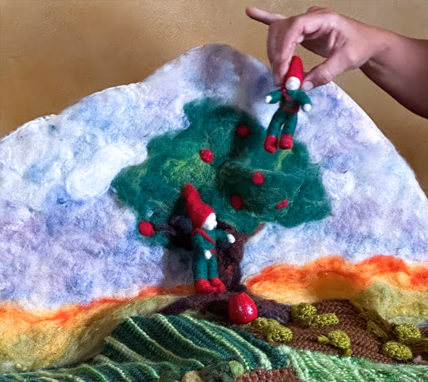 Hand arranging a felted wool artwork showing a tree and seasonal landscape.