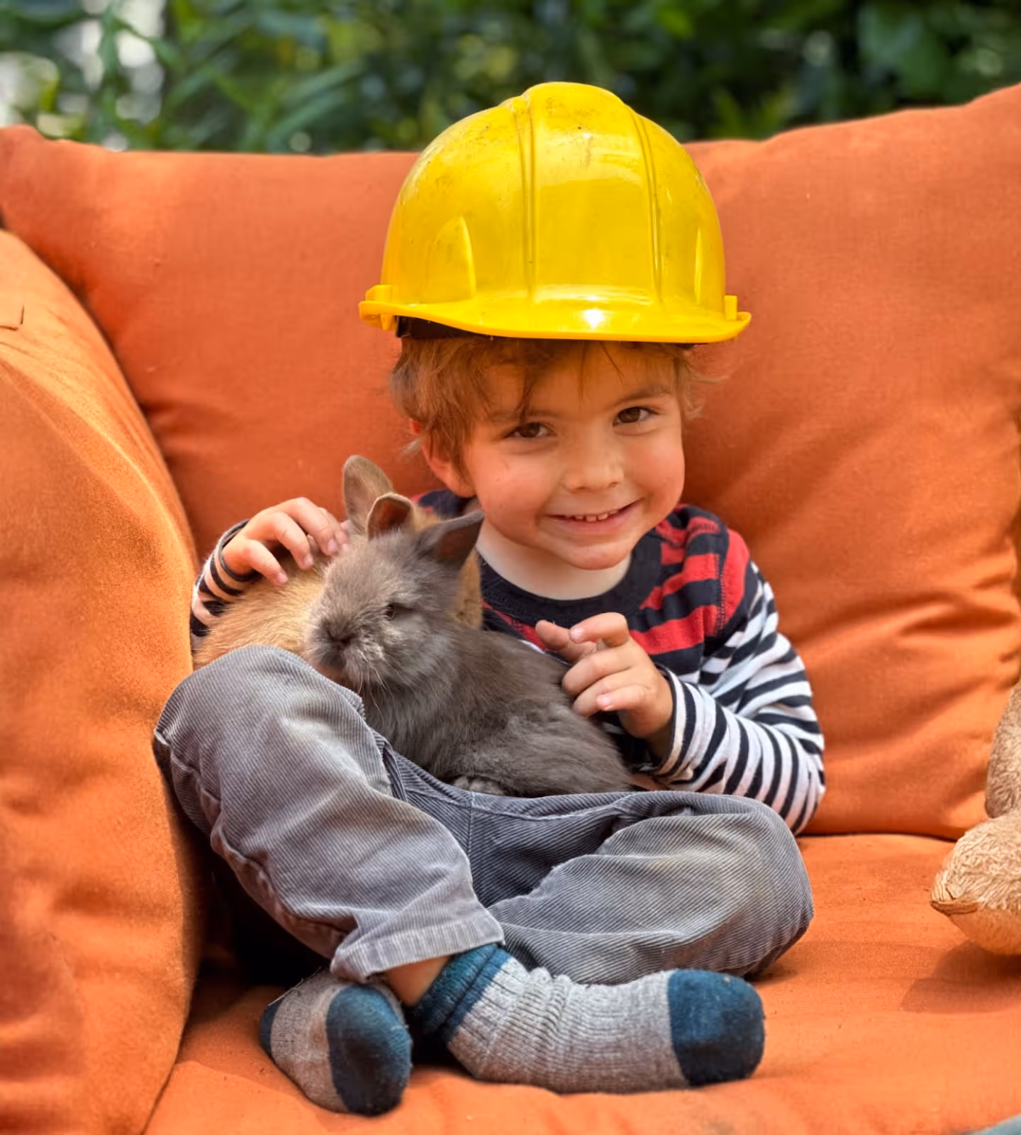 Child at Tree Sprites Preschool feeding leafy greens to two fluffy rabbits, showing care and connection with animals.