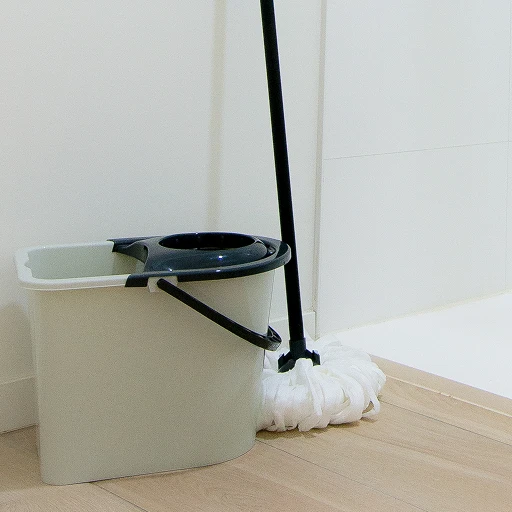 A bucket with a mop on the floor next to a mop holder.