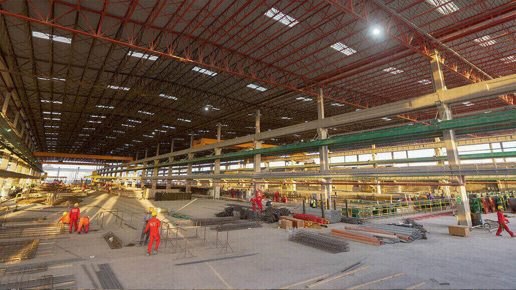 Large industrial warehouse with workers in red uniforms and construction materials scattered around.