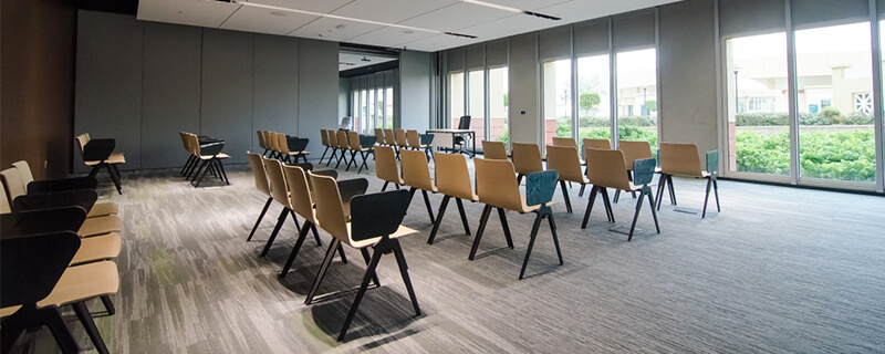 Empty modern conference room with rows of chairs facing a table near large windows.