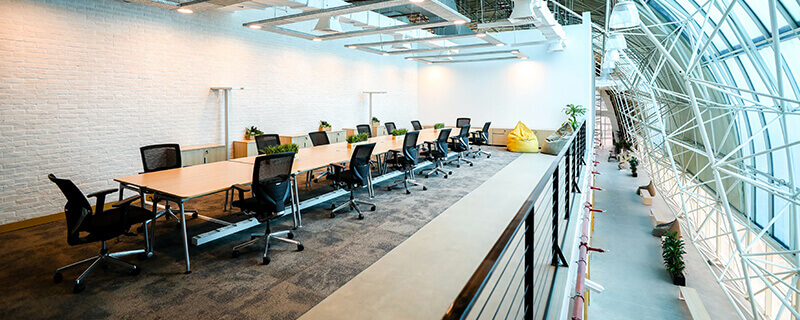 Modern conference room with long tables, black office chairs, bean bags, and large curved windows.