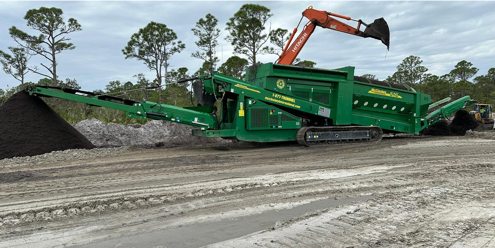 A green dump truck driving down a dirt road.