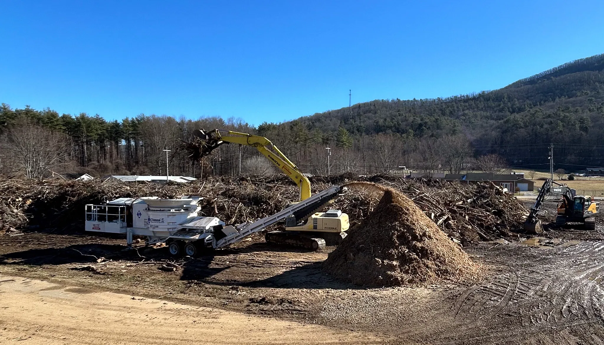 Excavator loading wood waste into a horizontal grinder for land clearing and wood recycling operations.