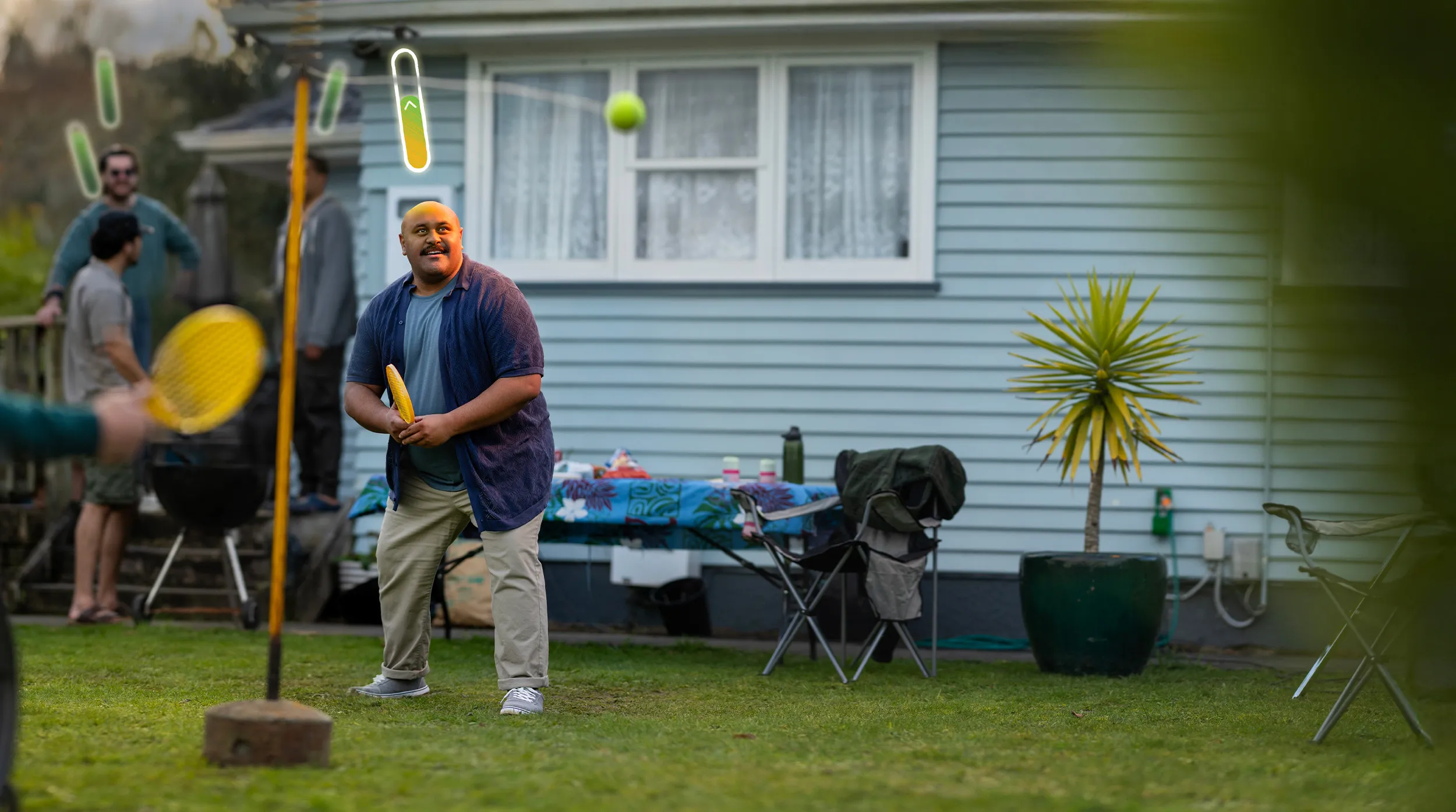 A man smiling and holding a yellow paddle, playing swingball in a suburban backyard with a glowing energy level indicator above his head symbolising a Top Up.