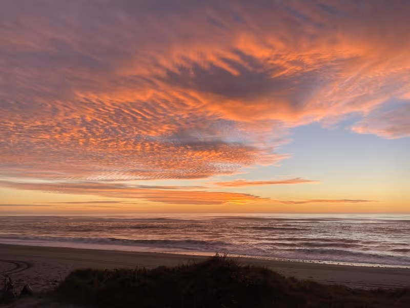 Sunset over a tranquil beach with vivid pink and orange cloud patterns in the sky, reflecting softly on the calm ocean waves, creating a serene atmosphere.