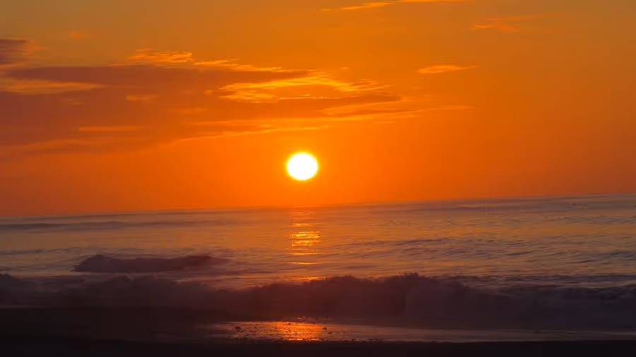 A vibrant sunset over a calm ocean, with vivid orange and pink hues. Soft waves roll in, creating a peaceful and serene atmosphere.