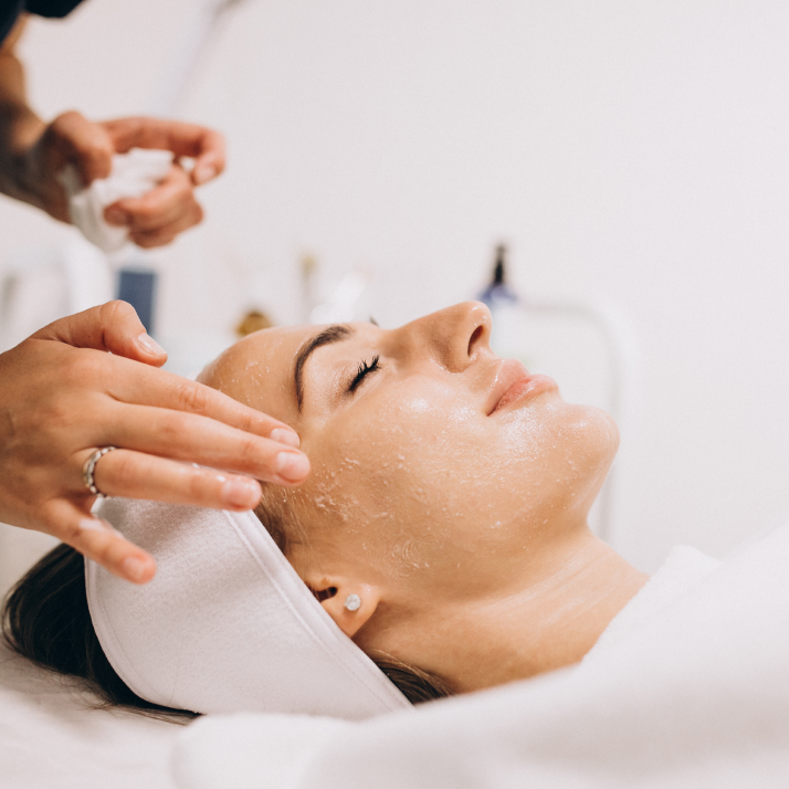 A woman with a towel on her head is applying a face cream.