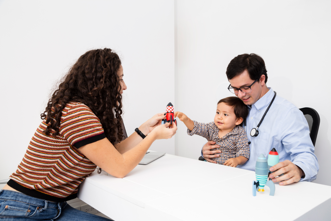 A doctor examines a baby's chest while a nurse looks on.