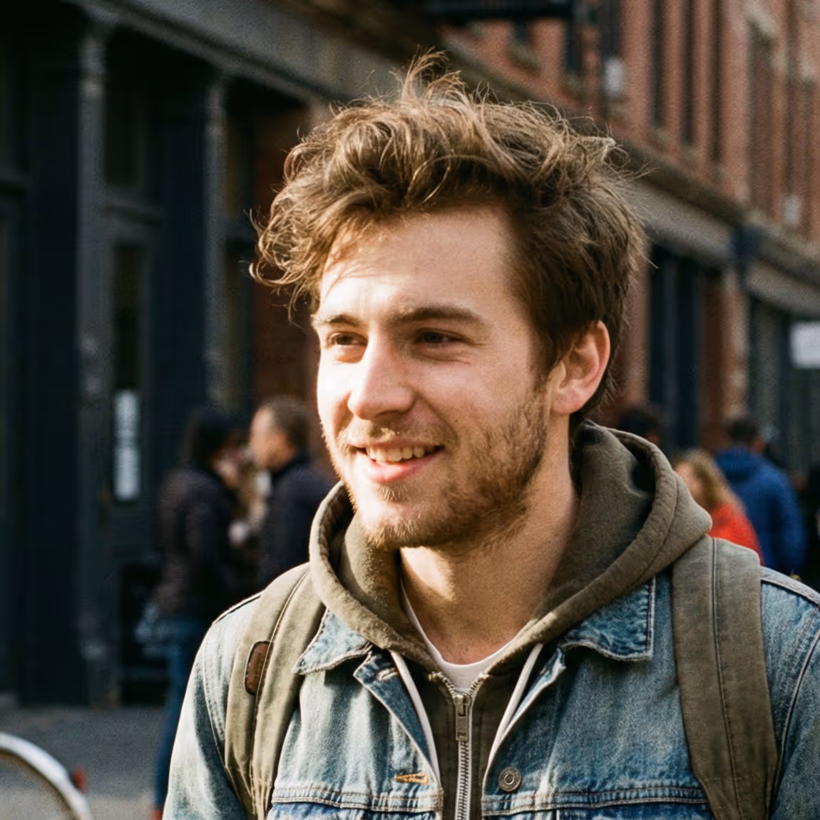 Smiling red-haired woman with curly hair wearing a denim jacket and striped shirt indoors.