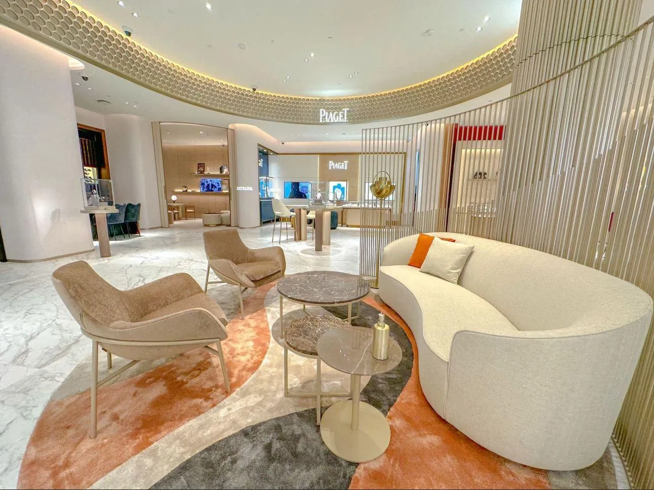 Luxurious lounge area with a curved white sofa, two beige armchairs, round marble side tables, and a colorful abstract rug in a high-end retail store.