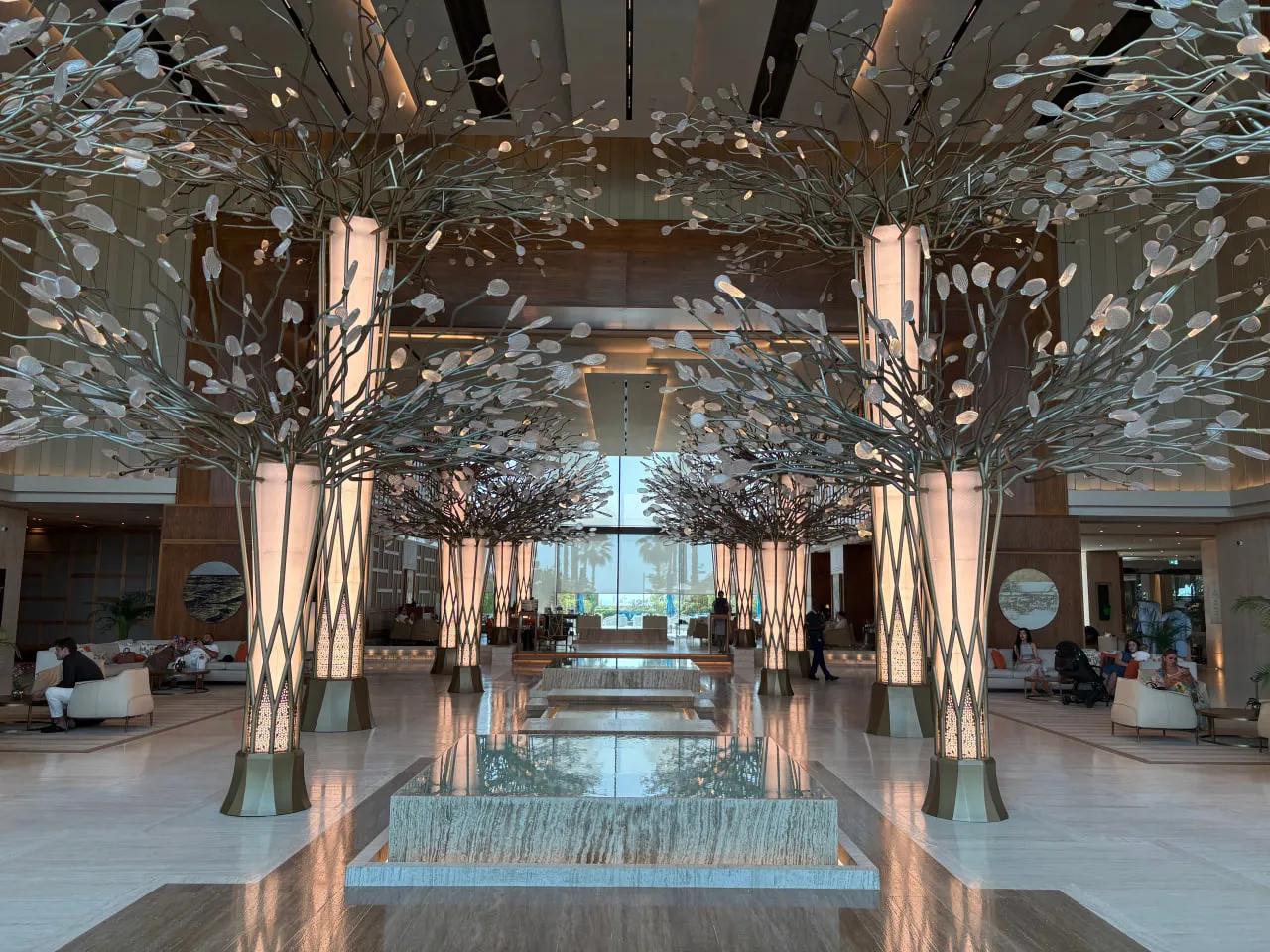 Spacious modern hotel lobby with artistic tree-like light fixtures lining a reflective water feature