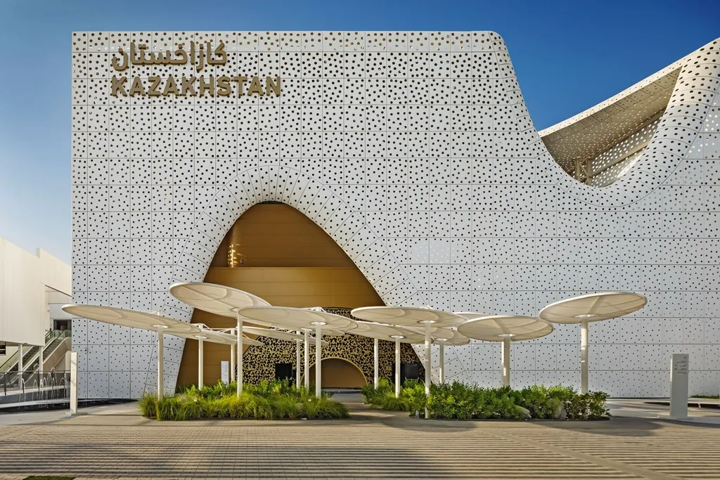 Modern Kazakhstan pavilion with perforated white facade and curved entrance arches at Dubai Expo 2020 under clear blue sky.
