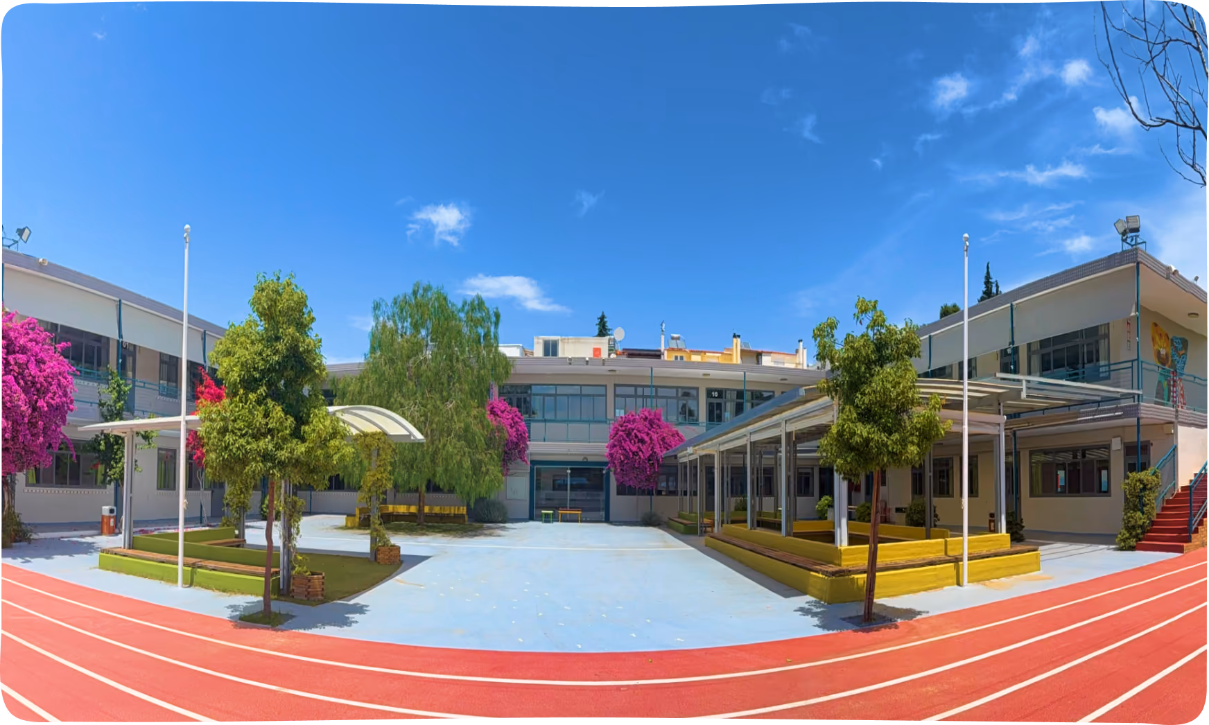 Panoramic view of a school courtyard with a red running track, colorful bougainvillea trees, and a two-story building in the background.