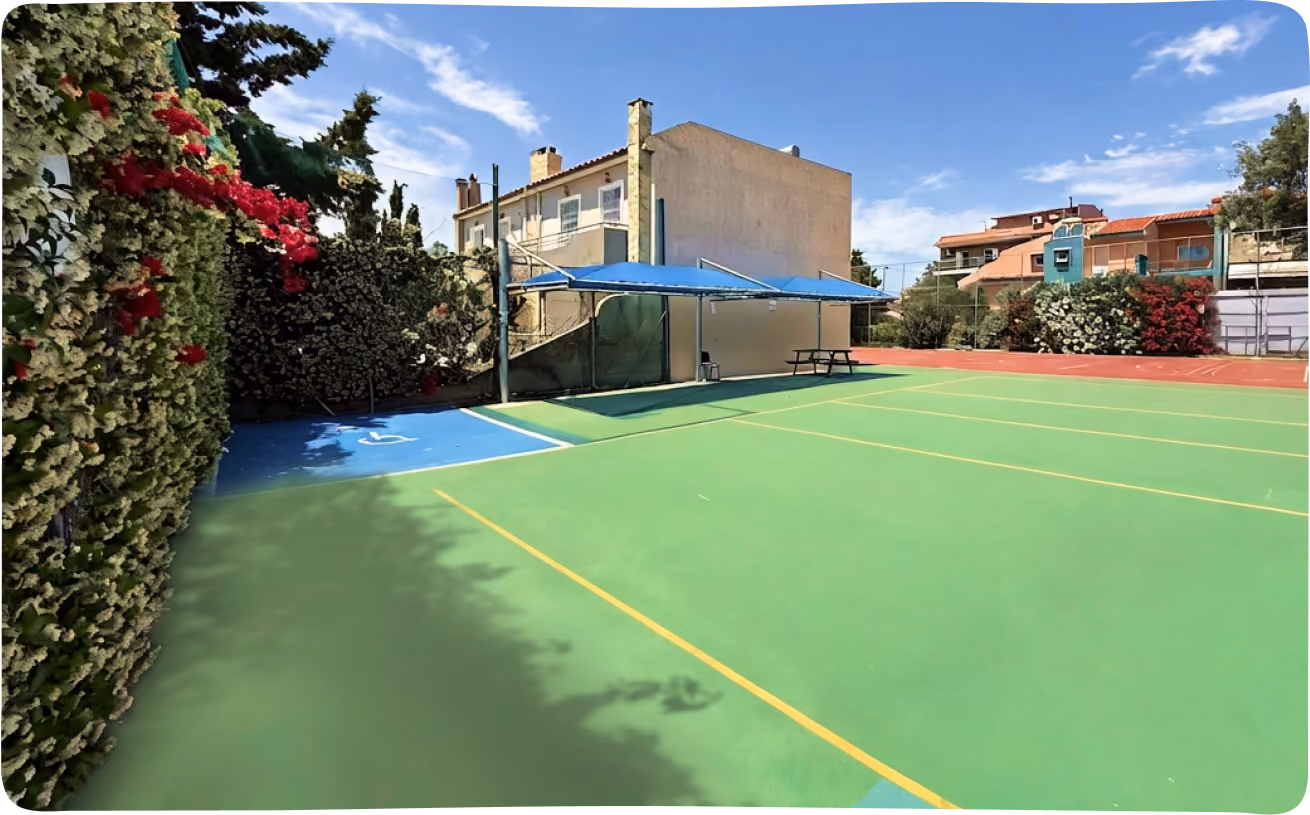 Green outdoor court with an accessibility-marked area, covered seating, and picnic table.