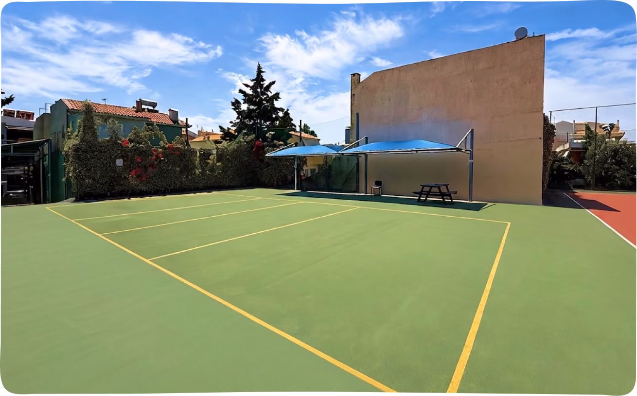 Green outdoor court with yellow lines next to a covered picnic area and shaded seating.