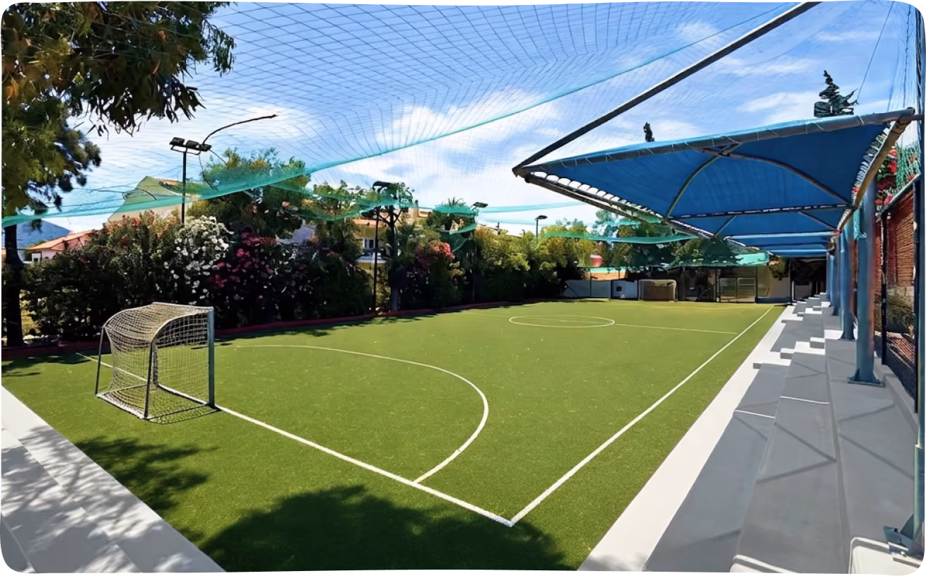 Artificial turf mini football field with a covered spectator area and overhead netting.