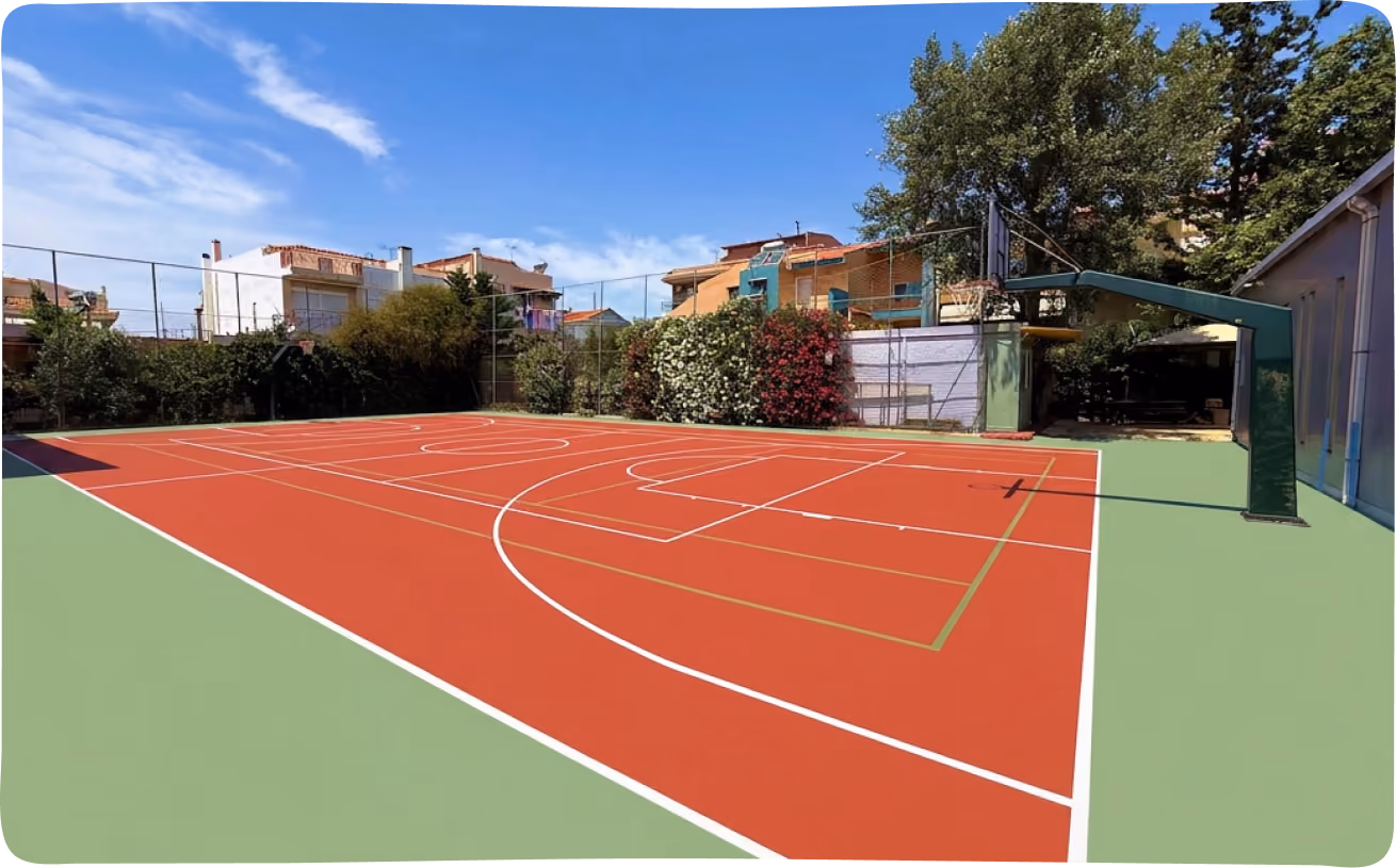 Outdoor basketball court with red and green flooring, surrounded by a chain-link fence and trees.