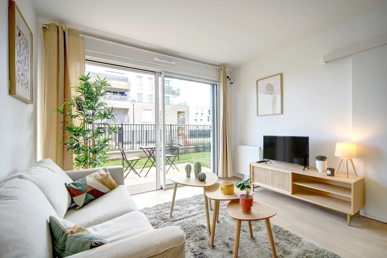 Séjour meublé d'un appartement Mobicap avec canapé, meuble TV et baie vitrée sur la terrasse