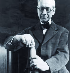 Frédérik Mähler en costume ouvrant une bouteille avec un tire-bouchon dans une pièce sombre.