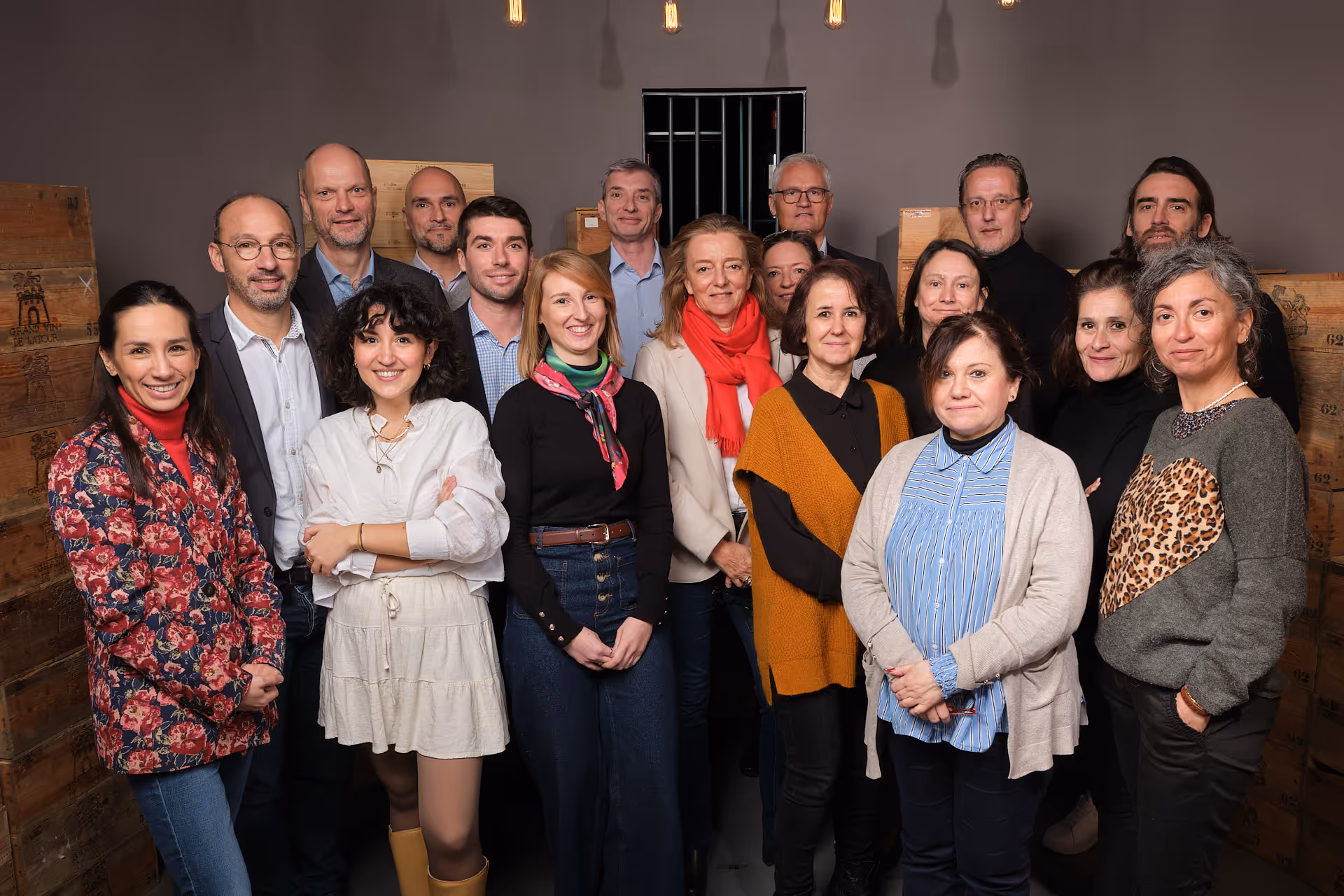 Groupe de dix-sept personnes posant ensemble devant des caisses en bois sous un éclairage intérieur chaleureux.