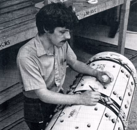 Man with mustache operating and marking a cylindrical control panel with buttons and switches.