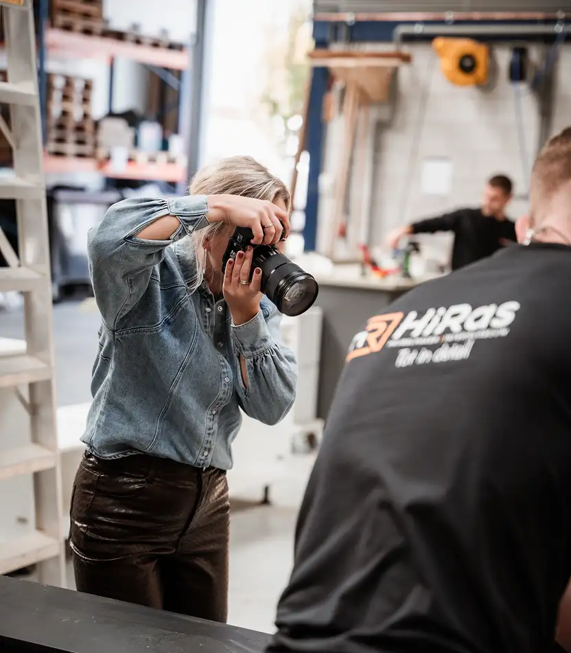 Vrouw met spijkerblouse maakt een foto met een professionele camera in een industriële werkplaats.
