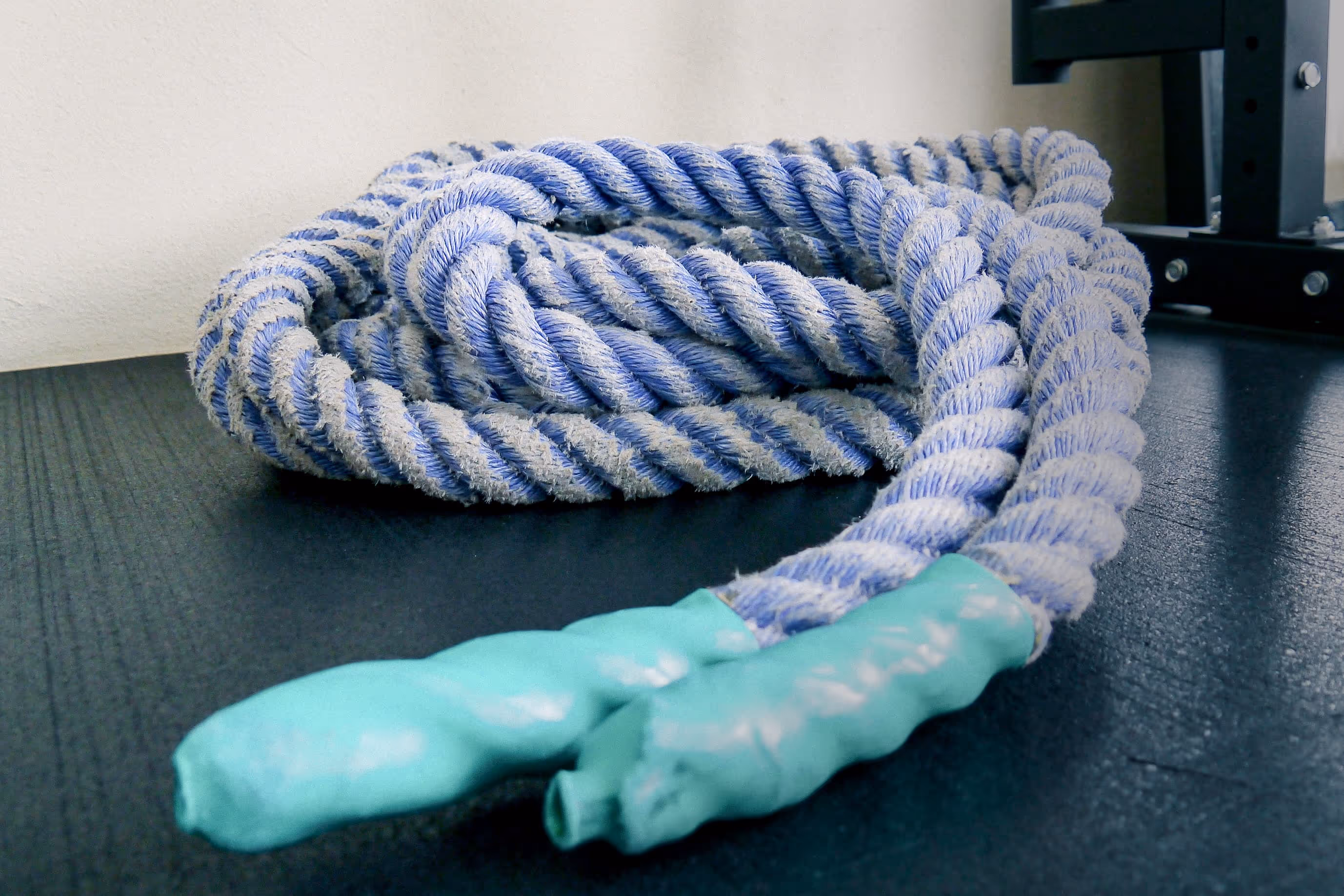 Nahaufnahme eines blau-weißen Battle Ropes mit türkisfarbenen Griffen auf dem Boden im Fitnessstudio