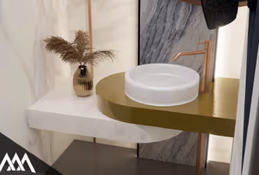 Modern bathroom sink setup with a round white basin, gold countertop, copper faucet, and a vase with dried pampas grass.