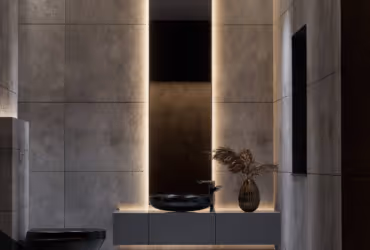 Modern bathroom with dark walls, illuminated recessed lighting, floating vanity with black vessel sink and decorative vase with dried plants.