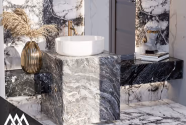 Modern bathroom with marble surfaces, a round white sink, gold faucet, decorative vase, and stacked books.