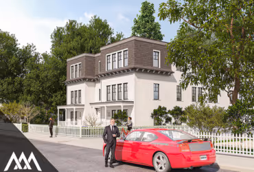 Man in suit standing beside a red sports car parked on a street with a large white house and trees in the background.