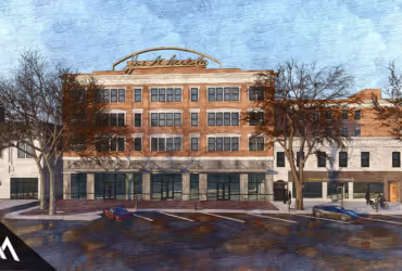 Four-story brick building with large windows and a rooftop sign, flanked by leafless trees and parked cars in front.