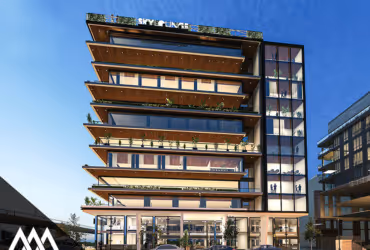 Modern multi-story building with large balconies and glass elevator shaft against a clear blue sky.