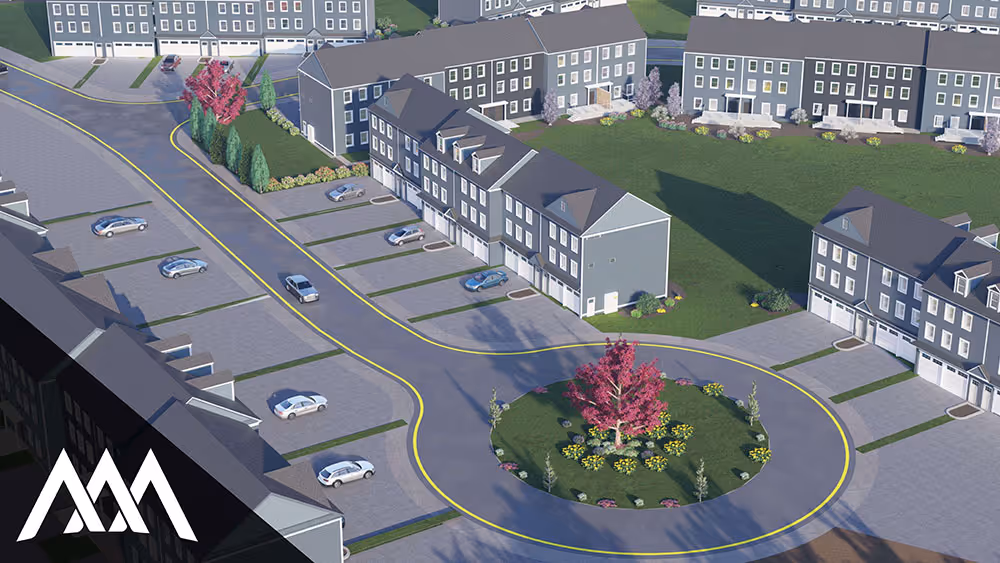 Aerial view of a suburban neighborhood with gray townhouses arranged around a circular road featuring a central green island with a pink-leaved tree and yellow flowers.