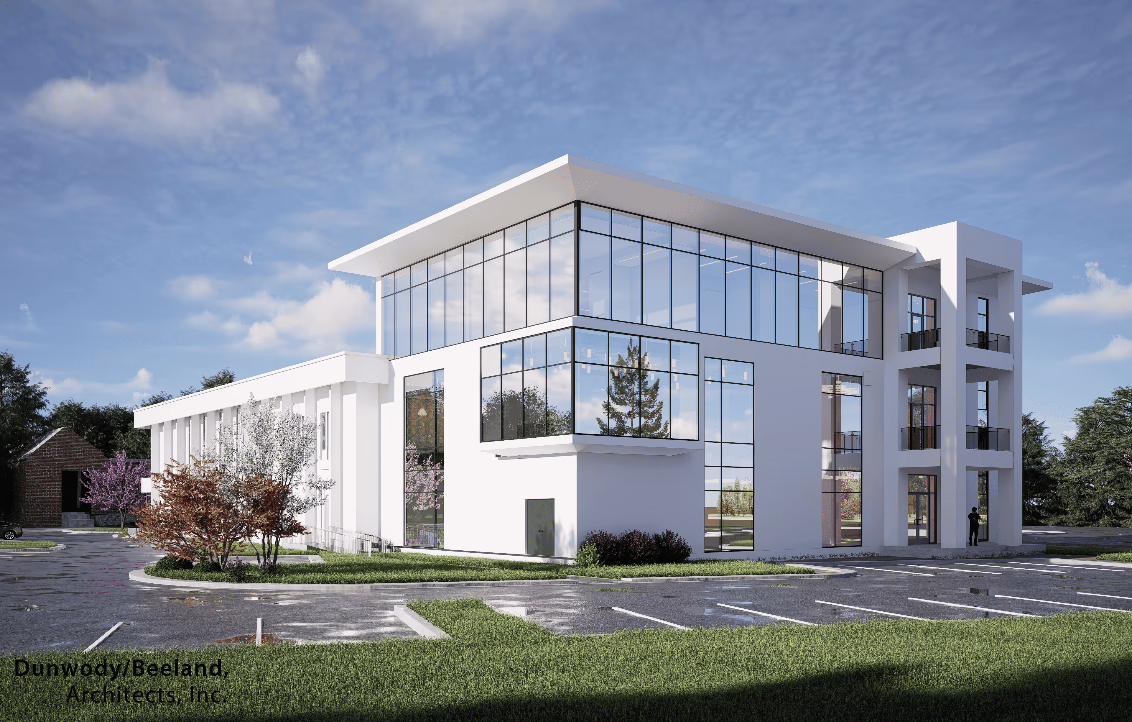 Modern three-story office building with large glass windows, surrounded by green lawns and parking spaces under a partly cloudy sky.