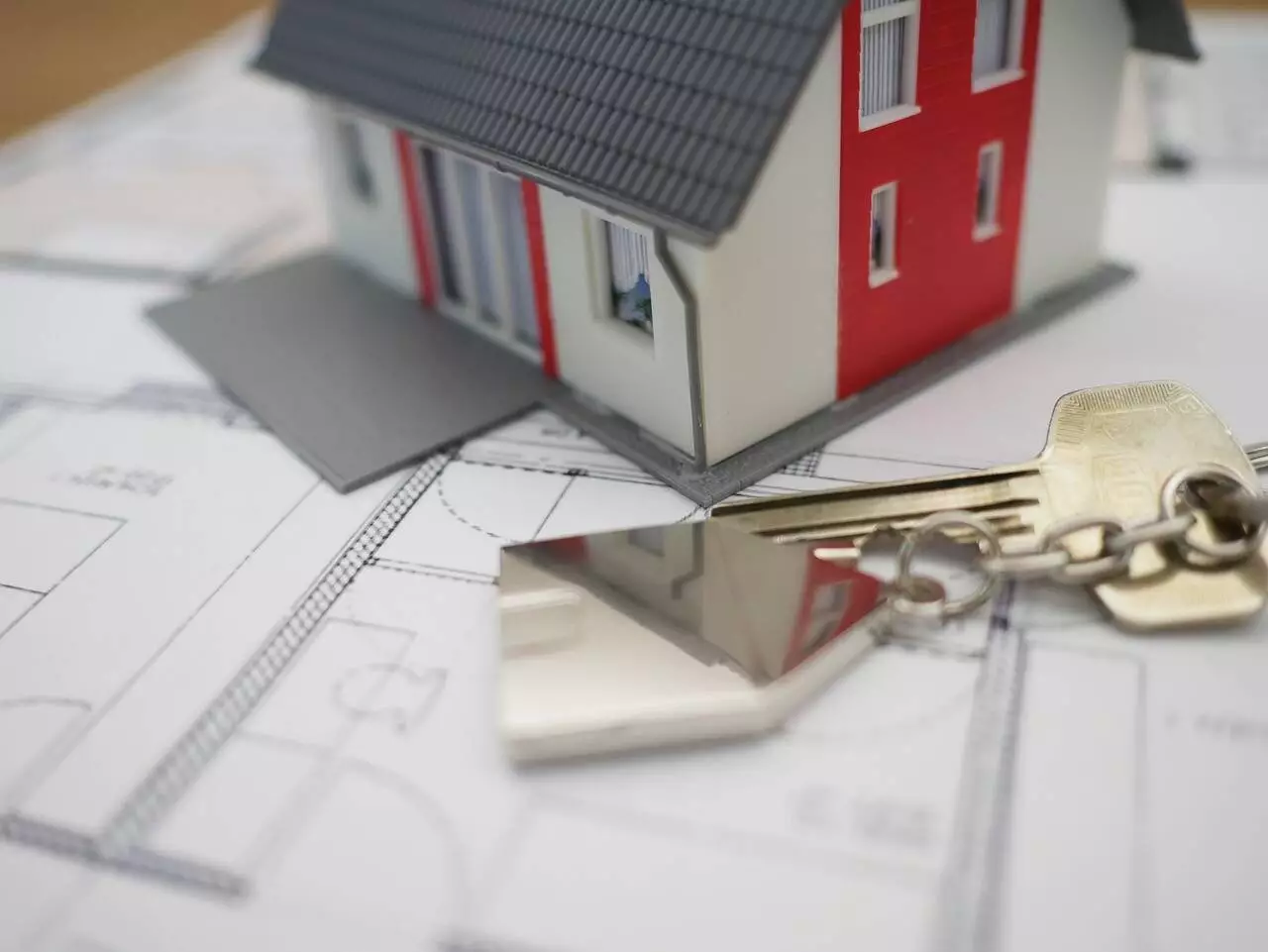 photo rapprochée d'une figurine de maison, de clés, posées sur un plan d'architect