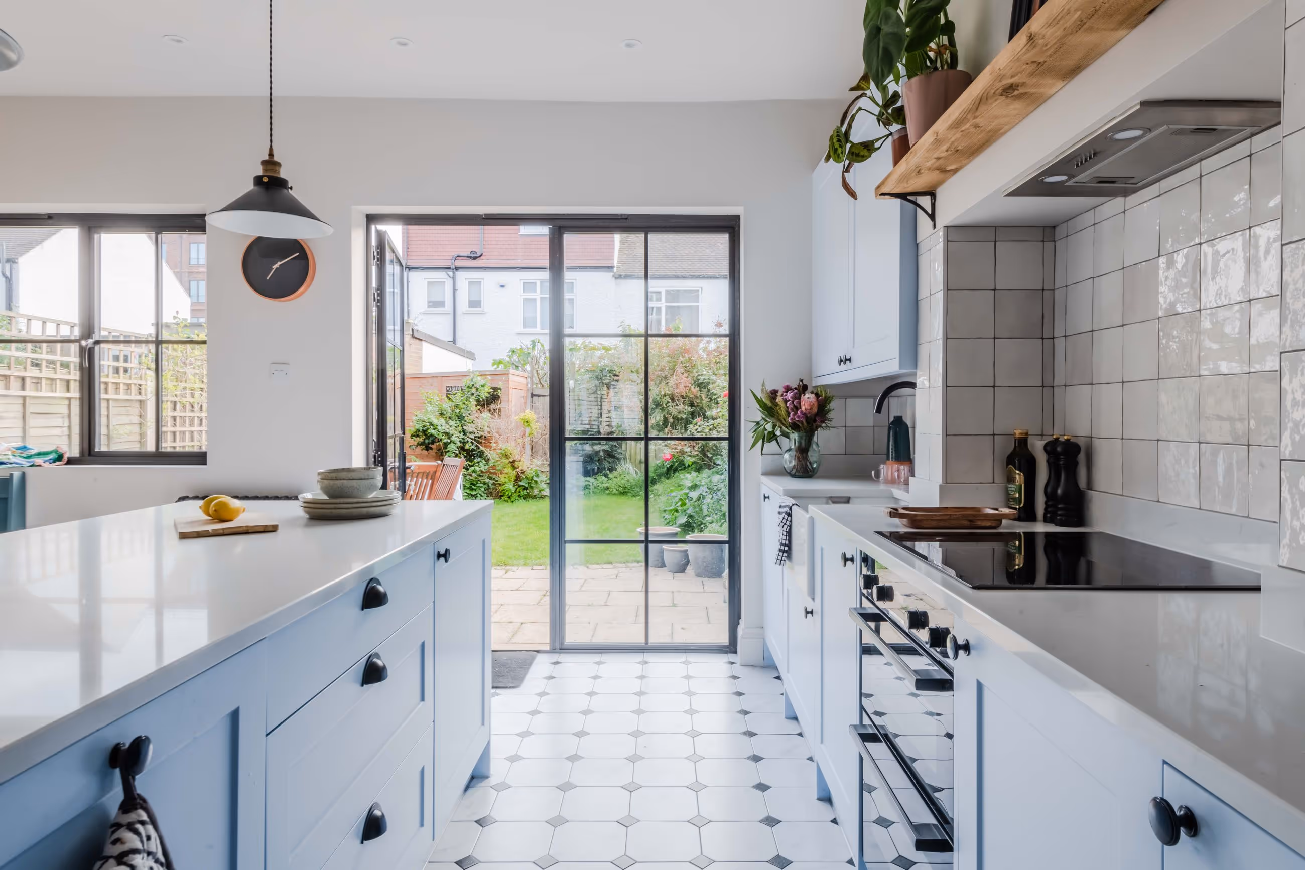 Bright kitchen with blue cabinets, white countertops, tiled backsplash, and glass doors opening to a garden.