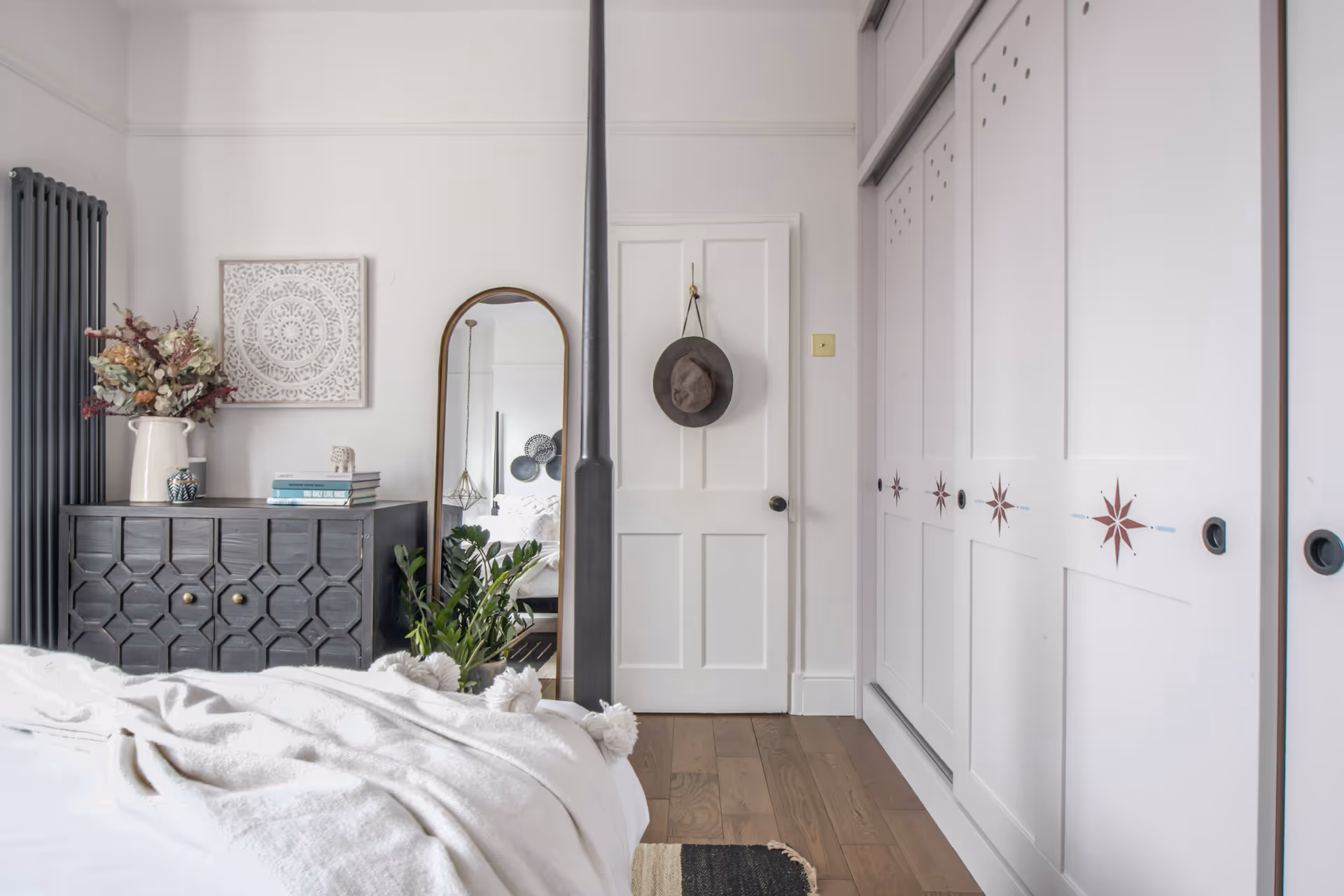 Bright bedroom corner with white door, tall floor mirror, gray dresser with decorative items, and white closet doors with star patterns.
