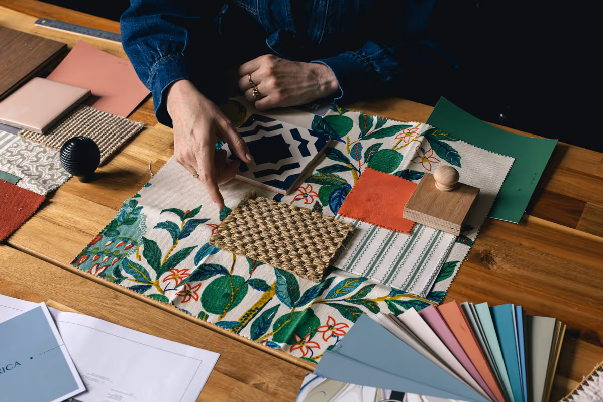 The founders of House of Norica, Eleanor and Jessica, sitting on sofas in a living room with framed art, a floor lamp, and window shutters in the background.