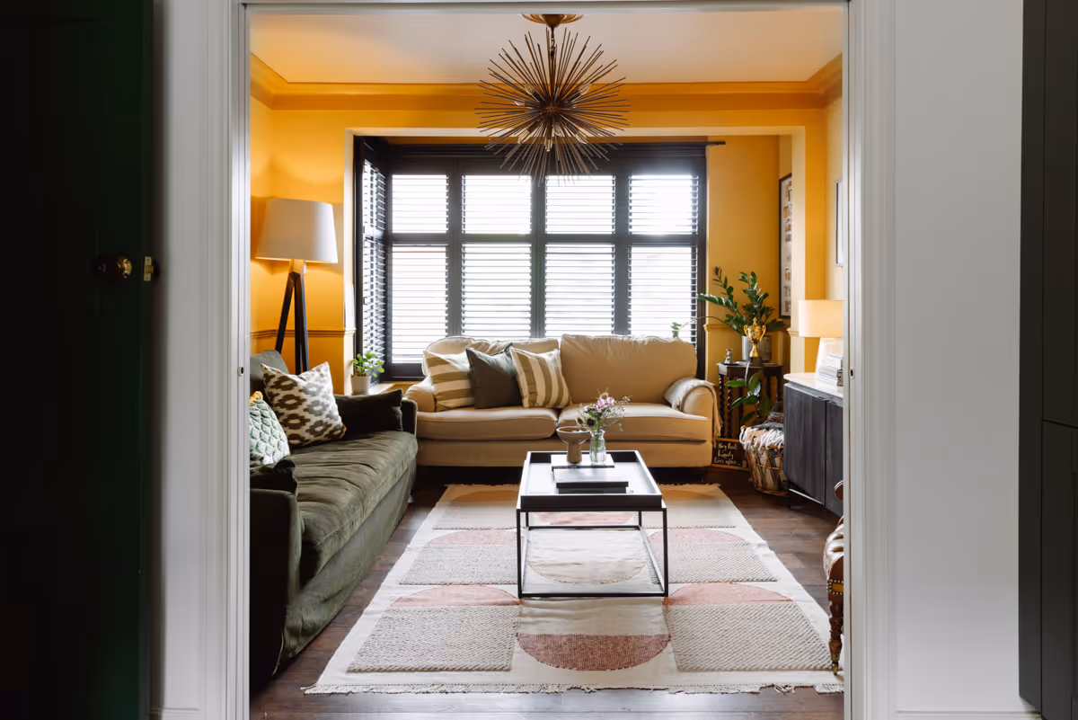 Preview of the Mitcham House project. A colour drenched mustard living room with dark wooden flooring and brass starburst light fixing.