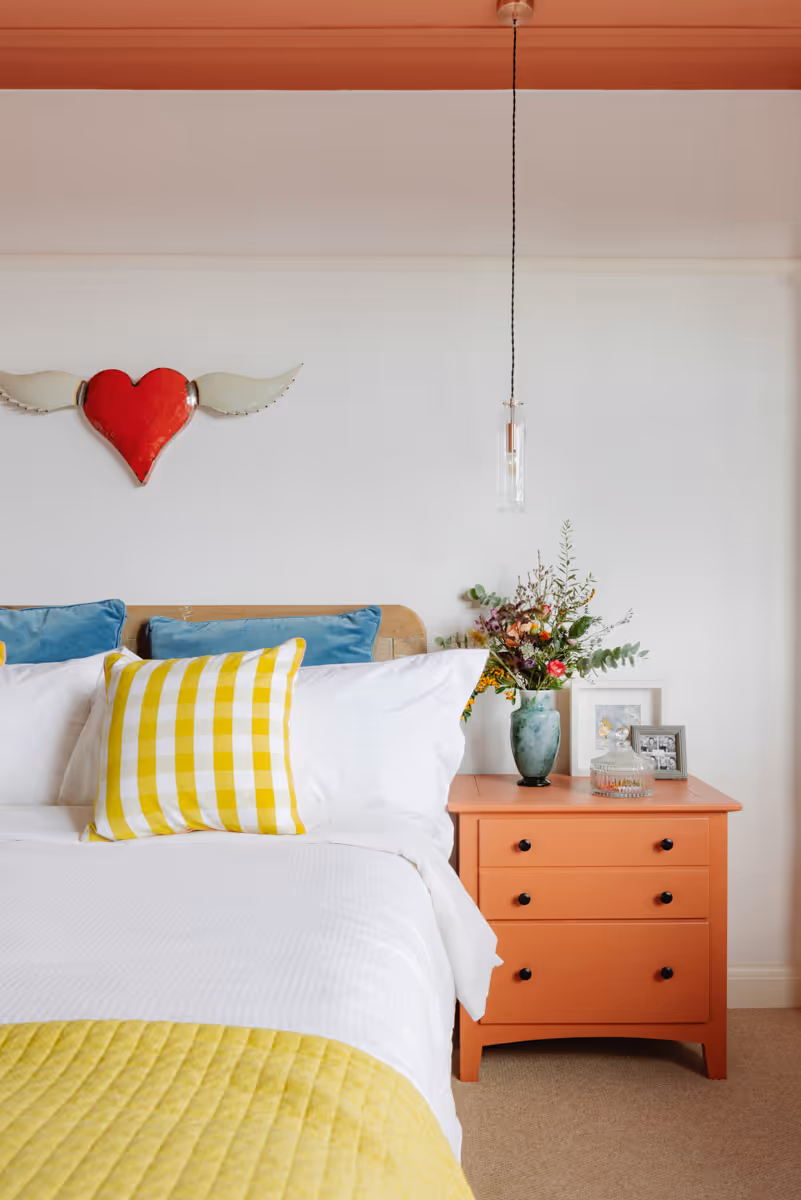 Preview of the South Lambeth Bedroom project. Light walls with contrast with a bright orange bedside table and colourful bed linen.