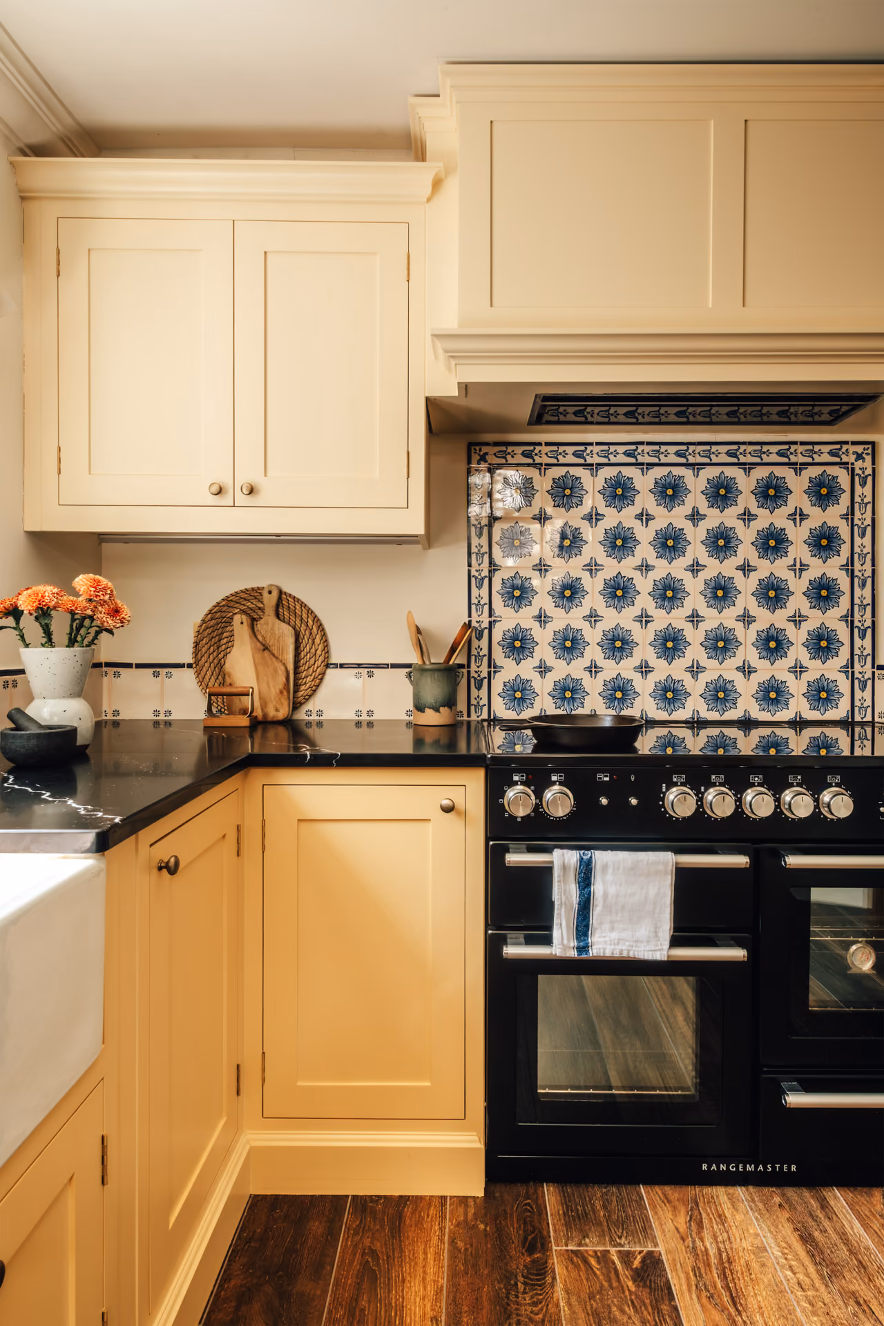 Modern kitchen with pink cabinets, terrazzo countertop island with woven chairs, loaf of bread, two wine glasses, and a pantry with a blue door.