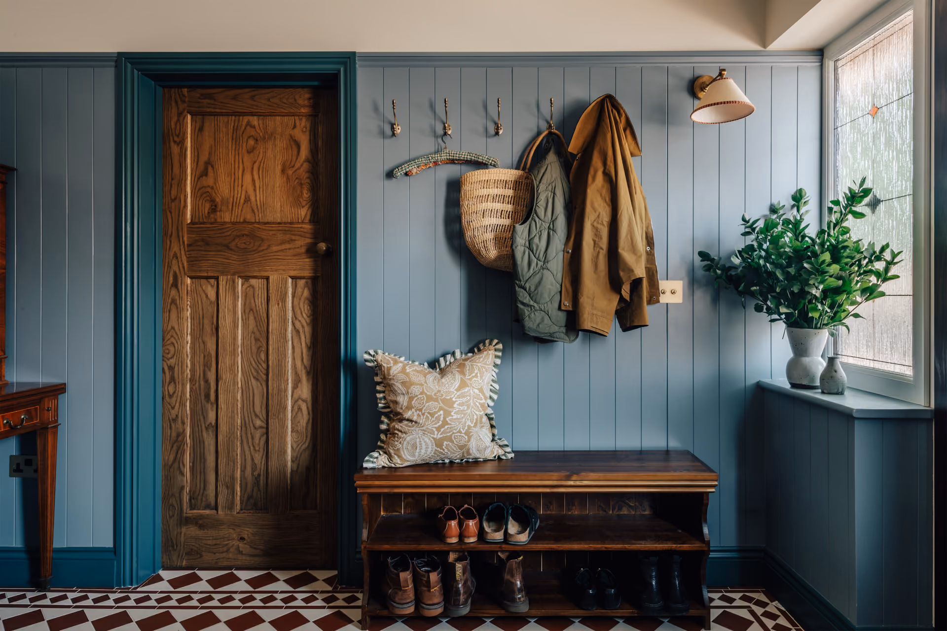 Living room with beige sofa, abstract blue and white painting, wooden coffee table with vase and candles, green-striped stool, indoor plant, and patterned cabinet with vase of branches.