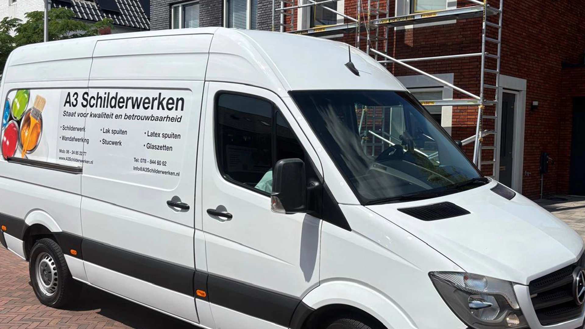 Witte bedrijfsbus van A3 Schilderwerken met reclamebestickering geparkeerd voor een woning met steiger.