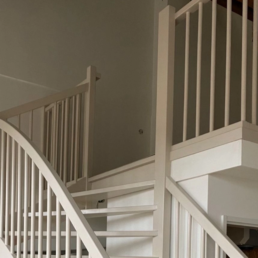 Wit geschilderde houten trap met balustrade in een lichte ruimte.
