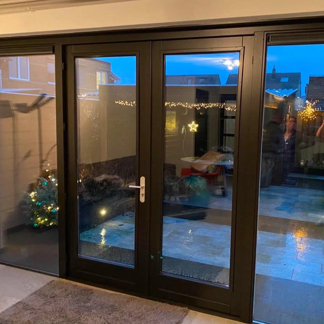 Zwart geschilderde houten schuifpui met grote ramen en uitzicht op een tuin in kerstsfeer.