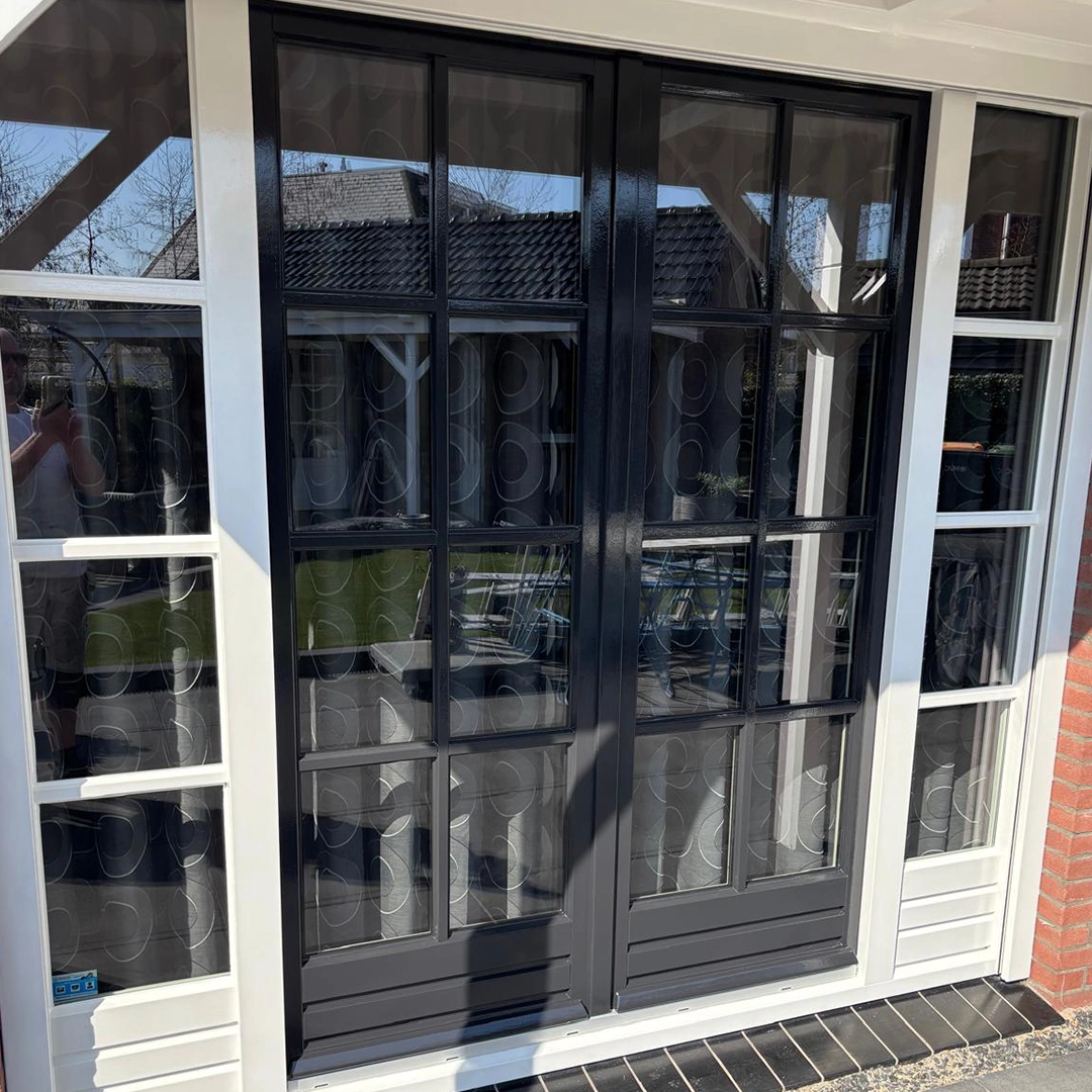 Dubbele openslaande deuren met zwart geschilderde kozijnen en glas-in-loodstijl, omlijst door witte kozijnen.